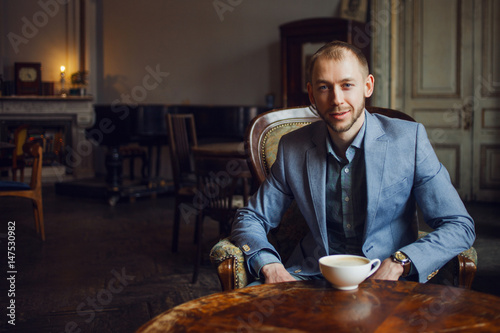 Young man sits and enjoys coffee in the morning. Portrait in the interior