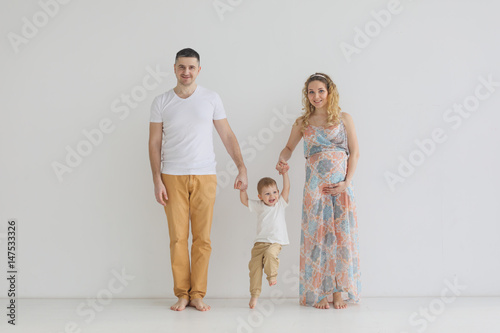 Pregnant family standing by the wall by the hand, holding hands, white room