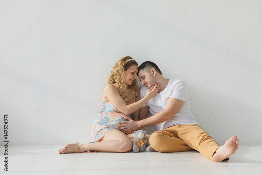 Pregnant family sitting on the floor embracing, holding hands, white room Pregnant family sitting on the floor embracing, holding hands, white room