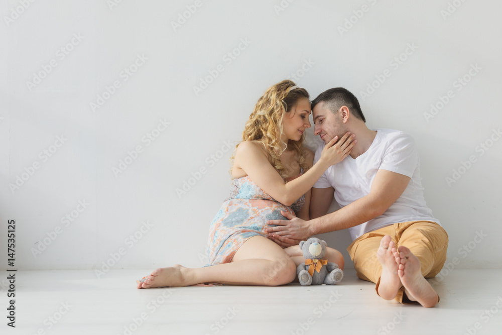 Pregnant family sitting on the floor embracing, holding hands, white room Pregnant family sitting on the floor embracing, holding hands, white room