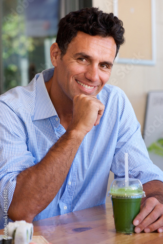 smiling middle age man sitting at table with cup of green juice