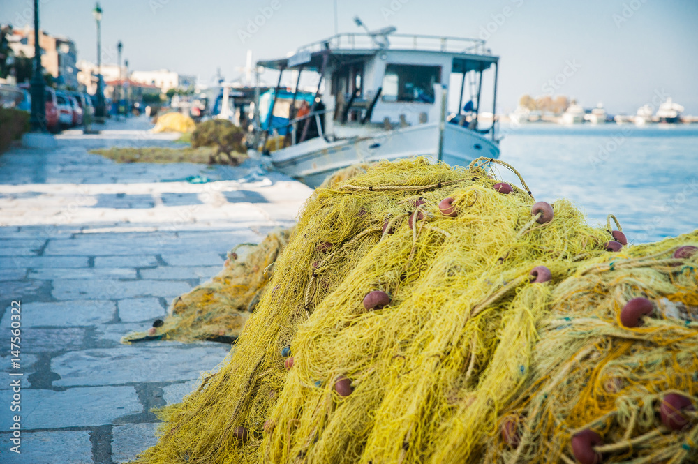 Folded fishing nets on the coast with white boat in background, Greece