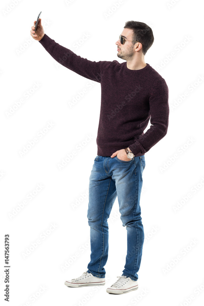 Side view of handsome casual man with sunglasses taking selfie with cell phone. Full body length portrait isolated over white studio background. Side view of handsome casual man with sunglasses taking selfie with cell phone. Full body length portrait isolated over white studio background.