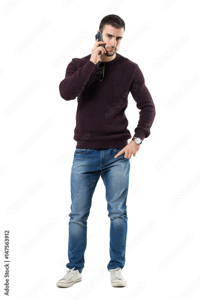 Angry young casual man talking on the phone looking at camera. Full body length portrait isolated over white studio background. Angry young casual man talking on the phone looking at camera. Full body length portrait isolated over white studio background.