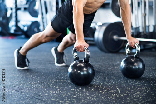 Unrecognizable fit man in gym doing push ups on kettlebells