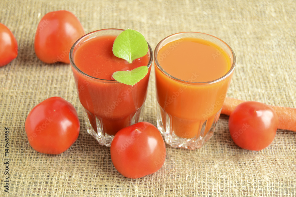 Tomato juice and juice carrot are poured in glasses. Tomatoes and carrots are located a row. Tomato juice and juice carrot are poured in glasses. Tomatoes and carrots are located a row.