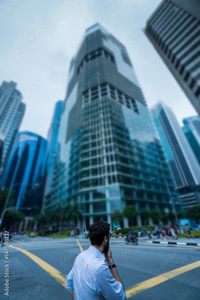 Fototapeta premium Back view of man standing on the street against modern skycrapers and sky background