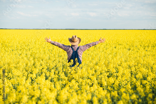 Agronomist standing in field of blooming cultivated rapeseed