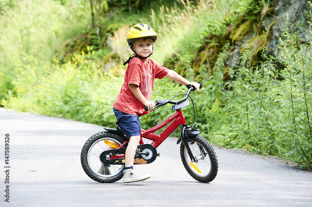 Young boy riding bicycle on a summer day at asphalt road. Bicycle path