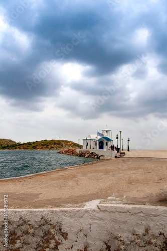 Small white chapel  on the coast under a dramatic blue sky in Greece © Stratos Giannikos