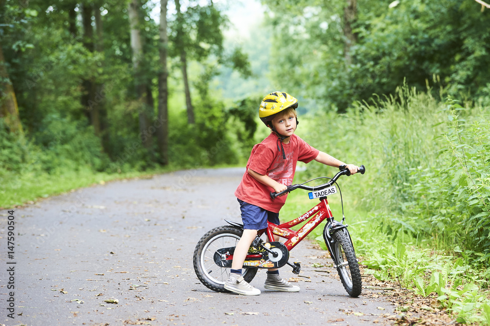 Child boy on a bicycle in the forest in summer. Boy cycling outdoors in safety helmet. Sun flare effect added