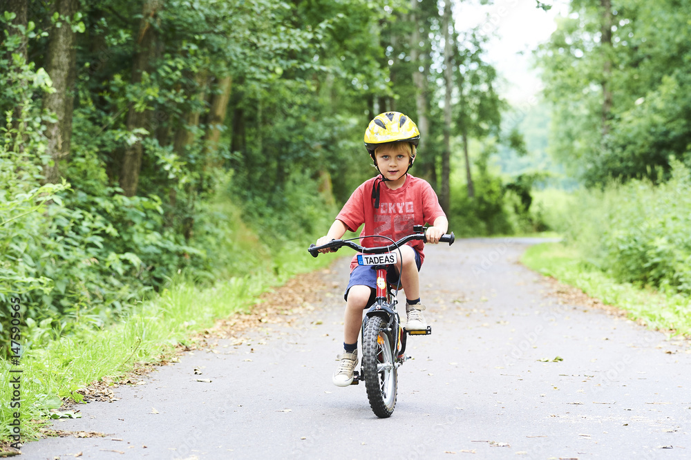Child boy on a bicycle in the forest in summer. Boy cycling outdoors in safety helmet. Sun flare effect added