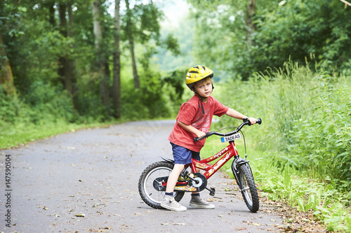 Child boy on a bicycle in the forest in summer. Boy cycling outdoors in safety helmet. Sun flare effect added
