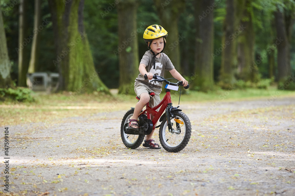 Child boy on a bicycle in the forest in summer. Boy cycling outdoors in safety helmet. Sun flare effect added Child boy on a bicycle in the forest in summer. Boy cycling outdoors in safety helmet. Sun flare effect added