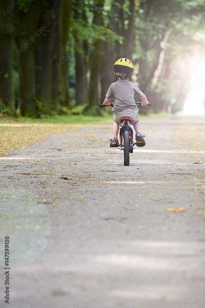 Obraz premium Child boy on a bicycle in the forest in summer. Boy cycling outdoors in safety helmet. Sun flare effect added