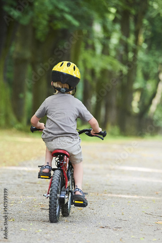 Fototapeta Naklejka Na Ścianę i Meble -  Child boy on a bicycle in the forest in summer. Boy cycling outdoors in safety helmet. Sun flare effect added