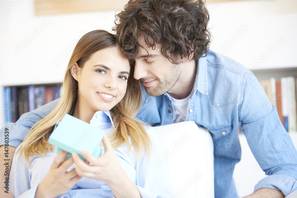 Lovely young couple with a surprise gift. Shot of a happy young woman opening the gift box while handsome smiling man standing behind her. Lovely young couple with a surprise gift. Shot of a happy young woman opening the gift box while handsome smiling man standing behind her.