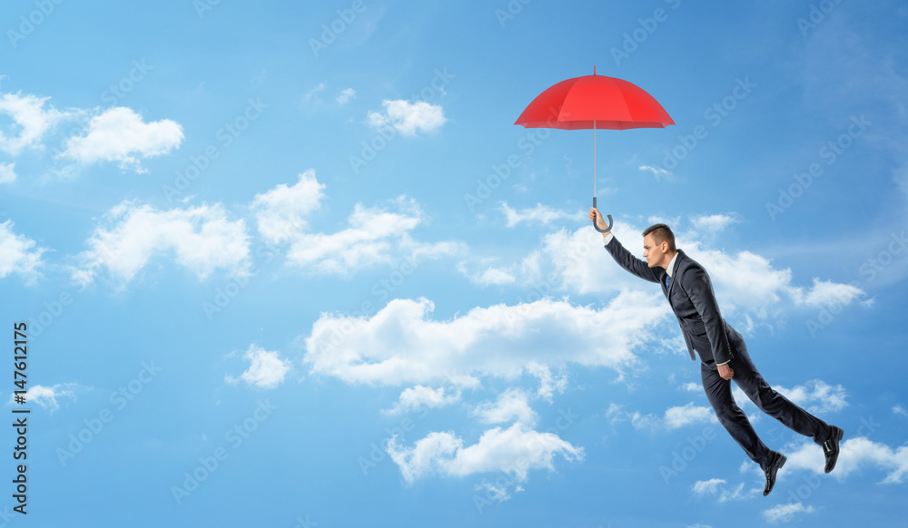 A businessman flying in the clouded sky and holding a red open umbrella. A businessman flying in the clouded sky and holding a red open umbrella.