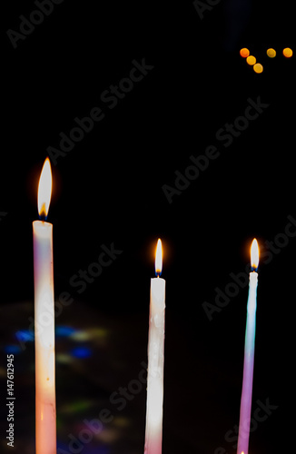 Three colorful festive candles on dark background. Sunlight filtered through the stained glass window reflected on the candles.