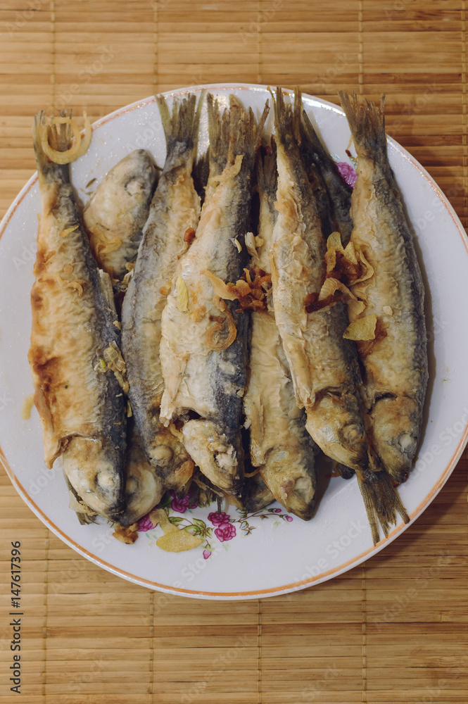Fried fish Baltic herring lies on a plate on a bamboo napkin.