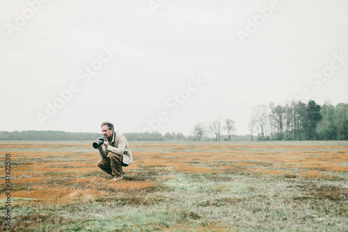 Nature photographer sitting down in grassy area holding camera. © ysbrandcosijn
