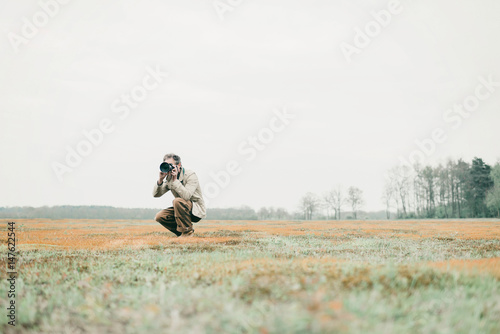 Nature photographer sitting down in grassy area taking pictures. © ysbrandcosijn