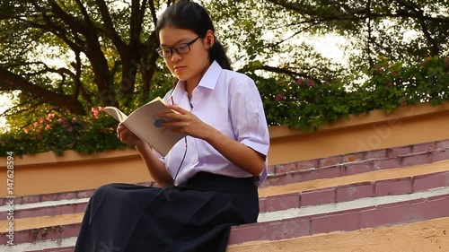 Thai girl student using smartphone to listening with earphone and reading a book photo