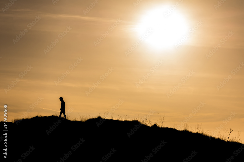 Man walking away from the sun on the hill. Artistic silhouette retro edit.