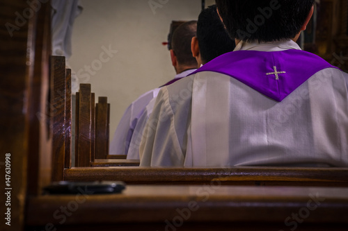 Priests sitting in church pews during mass or prayer. Artistic retro vintage edit.