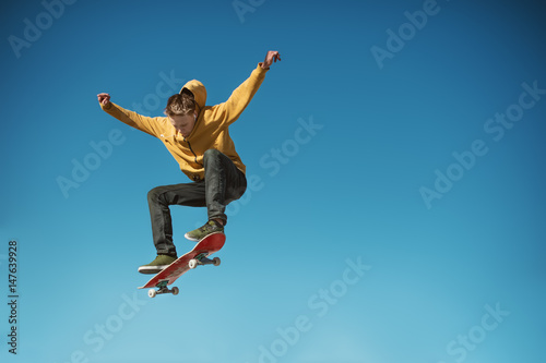A teenager skateboarder does an ollie trick on background of blue sky gradient photo