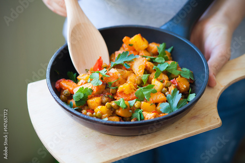 Woman holds a frying pan with vegetable stew on a cutting Board and pomeshivat spoon. Healthy eating.