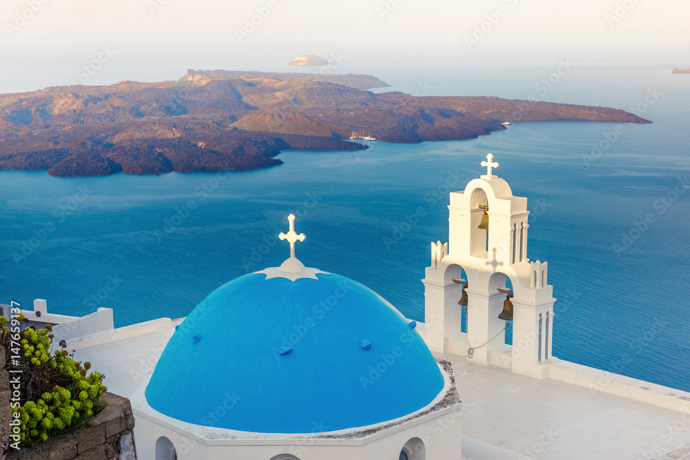 Blue dome church of Santorini island, Greece, Fira village. Island in background, Morning scenery.