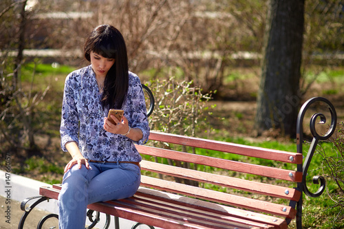 Beautiful Asian girl sitting on a bench in the park reading a message on the phone