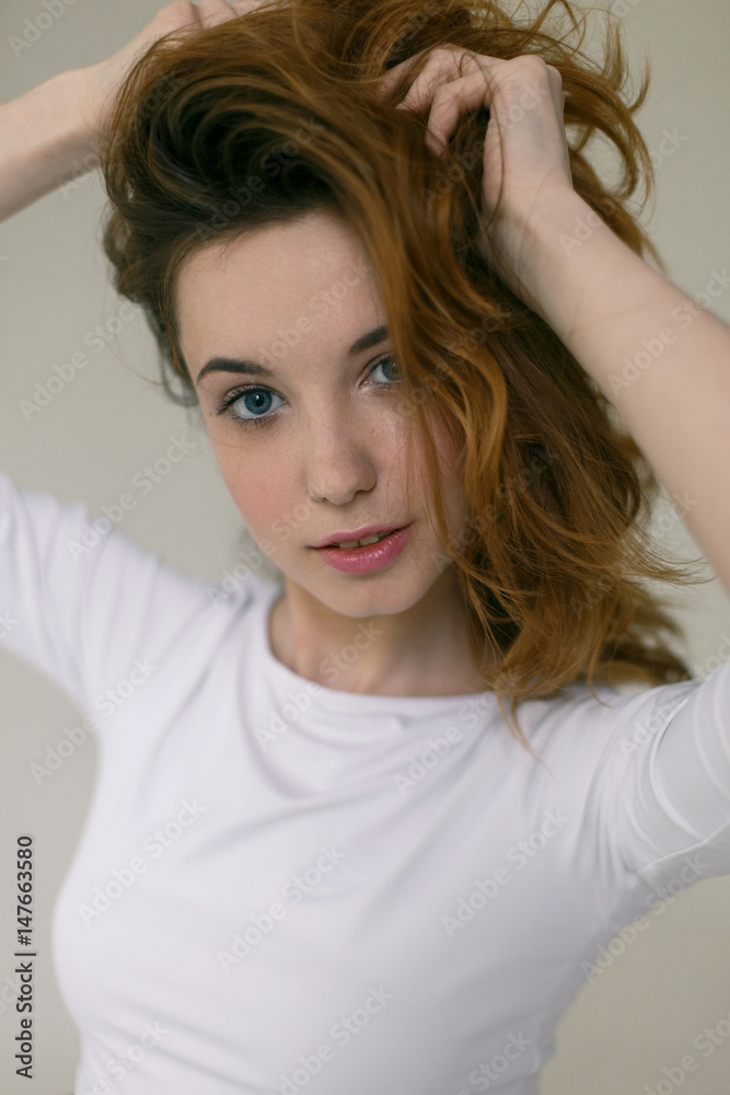 Closeup portrait of young girl with blue eyes beat hands hair on a light background Closeup portrait of young girl with blue eyes beat hands hair on a light background