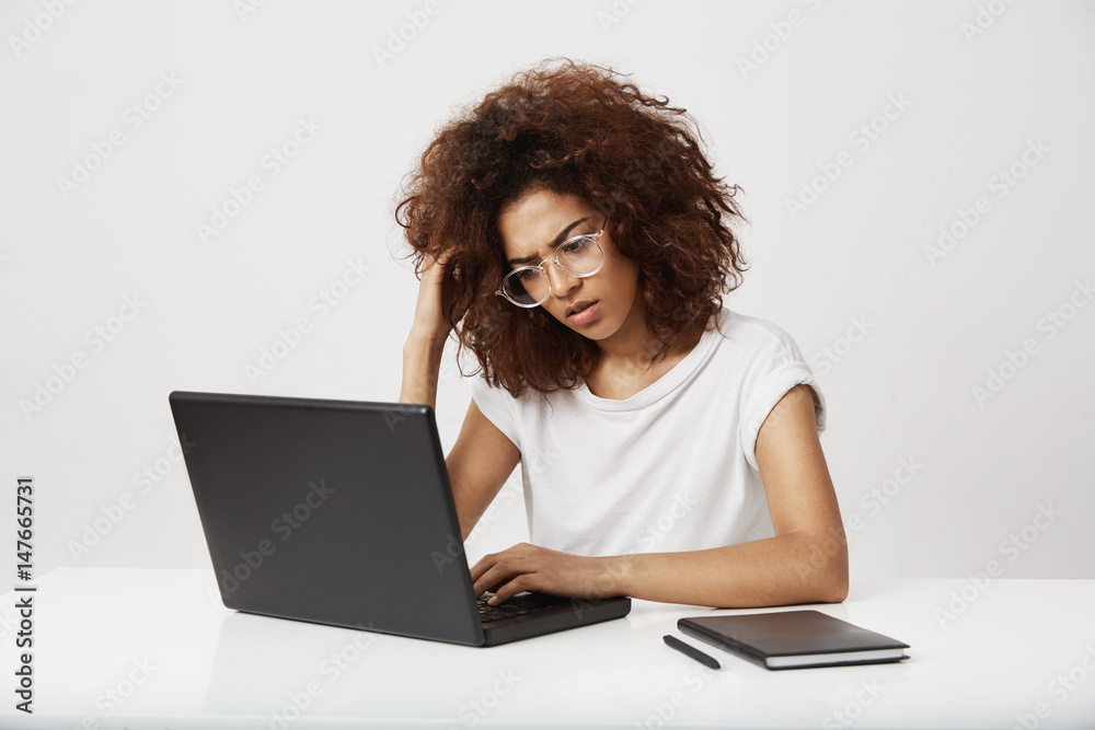 Tired and ucertain young african fashion design student thinking on her study working at laptop on business plan of future brand. Outstanding screenwriter in her twenties on white background. Tired and ucertain young african fashion design student thinking on her study working at laptop on business plan of future brand. Outstanding screenwriter in her twenties on white background.