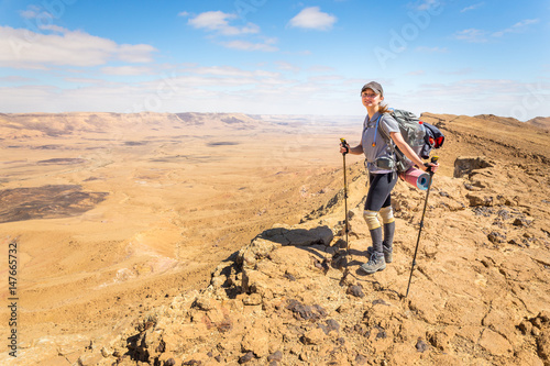 Young woman happy cheerful tourist backpacker standing  desert mountain edge