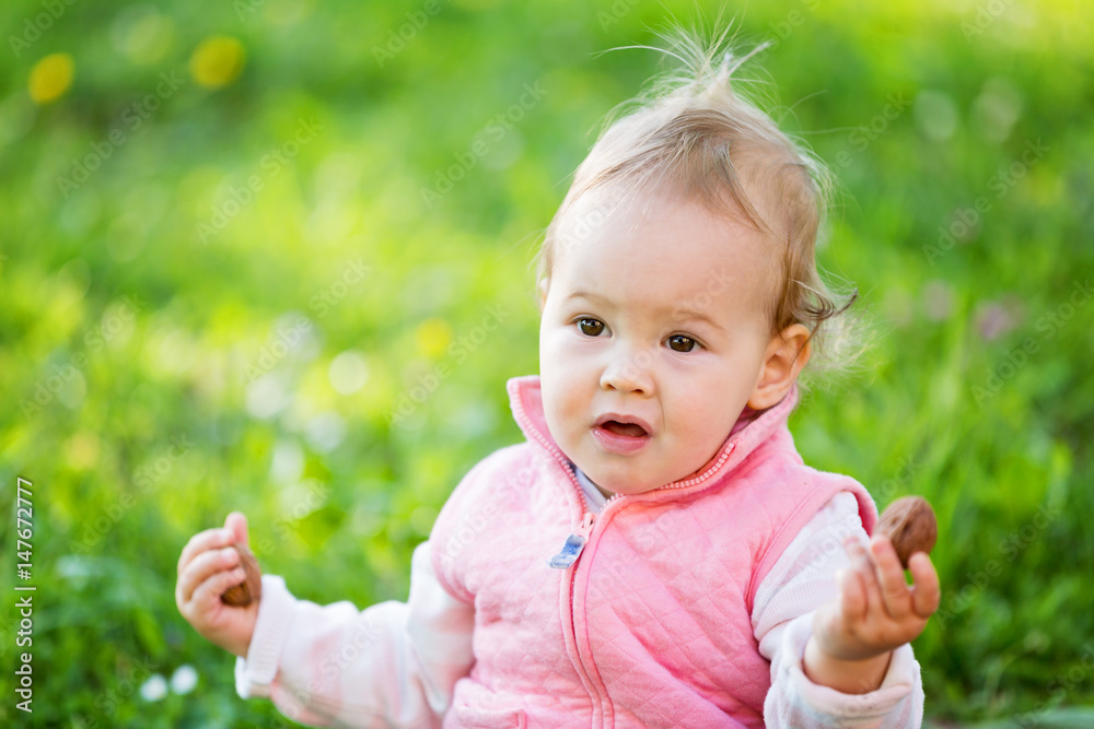 One year old baby sitting on the grass and holding a walnut in her tiny hand One year old baby sitting on the grass and holding a walnut in her tiny hand