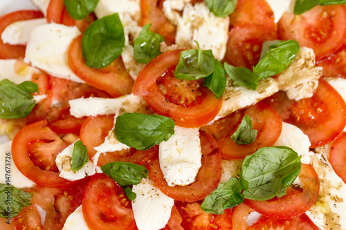Tomato and mozzarella salad with basil leaves, sprinkled with pepper, olive oil and acceto balsamico on the white plate