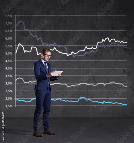 Businessman with smartphone standing on a diagram background. Business, finance, investment concept.