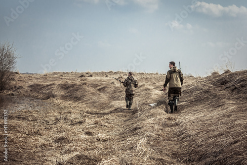 Hunting scene with men hunters with shotguns exploring rural area during hunting season