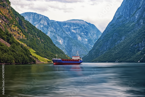 Norwegian fjord surrounded by mountains with sailing ship in a cloud summer day horizontal frame