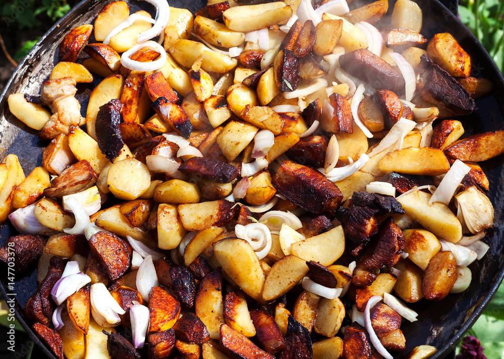 Beef meat stewed with potatoes on barbecue. Slice potatoes are prepared on the grill on sunny day. Close up. Culinary concept. Beef meat stewed with potatoes on barbecue. Slice potatoes are prepared on the grill on sunny day. Close up. Culinary concept.
