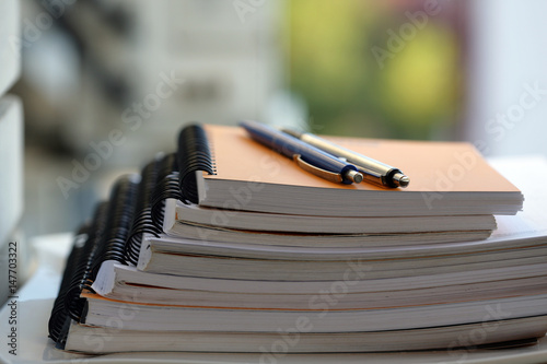 Stack of ring binder notebooks in horizontal order with two pens on the top.
