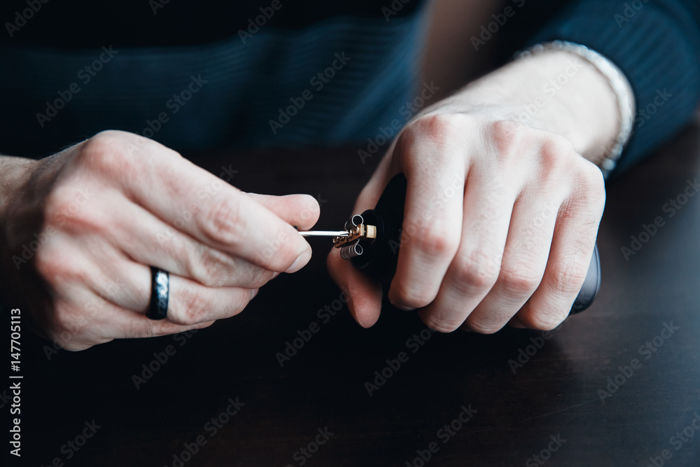 master man sets the coil with a screwdriver. Vape,electronic cigarette over a dark background. master man sets the coil with a screwdriver. Vape,electronic cigarette over a dark background.