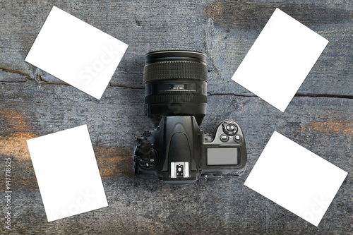 Modern camera placed on wooden desk surrounded with empty templates for photos, mockup photo