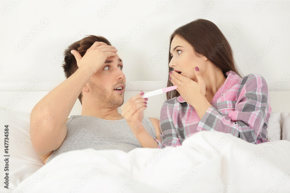 Surprised couple lying in bed with pregnancy test