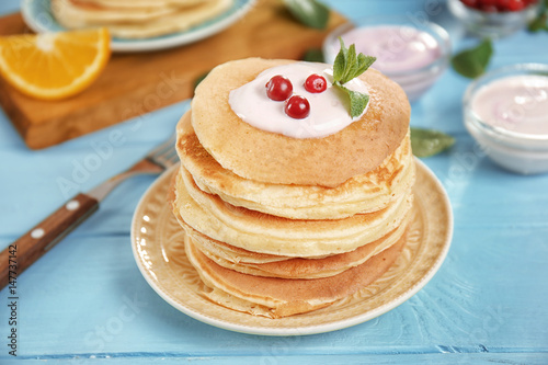 Plate with delicious pancakes, yogurt and cranberry on blue table