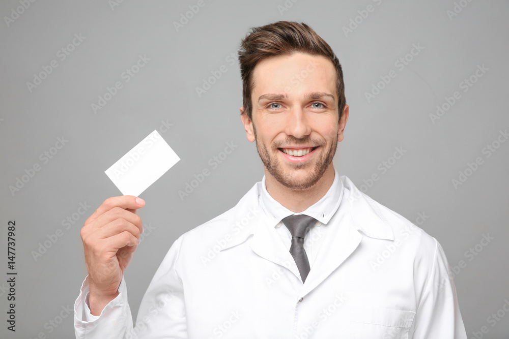 Handsome young man with business card on grey background