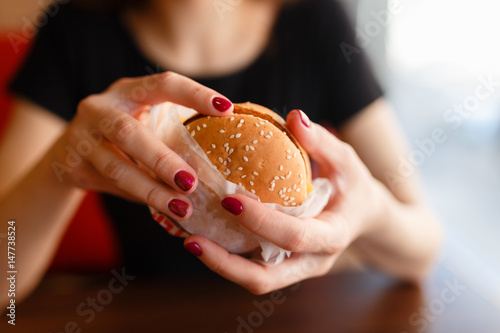Young girl holding in female hands fast food burger  american unhealthy calories meal on background  mockup with copy space for text message design  hungry human with grilled hamburger front view