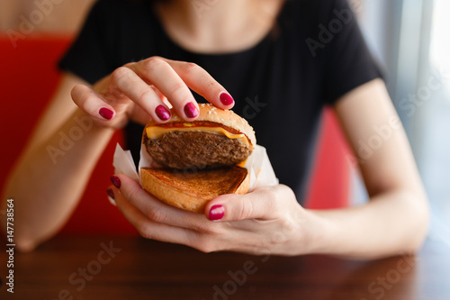 Young girl holding in female hands fast food burger and shows what he is made of  with copy space for text message or design  hungry human with grilled hamburger front view.